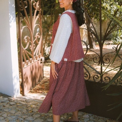 Mulher com conjunto de colete e saia vermelhos com padrões brancos, blusa branca e lenço vermelho na cabeça em ambiente exterior