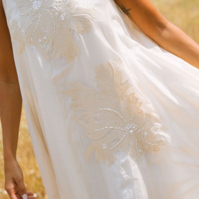 Vestido branco com bordados florais bege e pérolas, tecido leve, ambiente ao ar livre