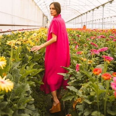 Mulher com vestido rosa-choque num viveiro de flores amarelas e cor-de-rosa