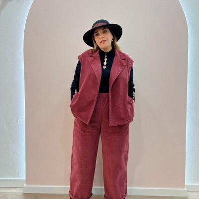 Mulher com conjunto vermelho aveludado, blusa preta e chapéu preto em ambiente interior