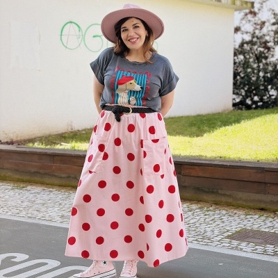 Mulher a usar chapéu rosa, t-shirt cinzenta com estampa de cachorro, saia rosa com bolinhas vermelhas e ténis cor-de-rosa