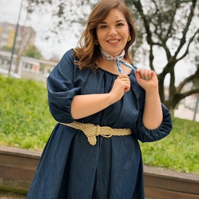 Mulher com vestido azul-escuro, cinto bege e cachecol floral ao ar livre