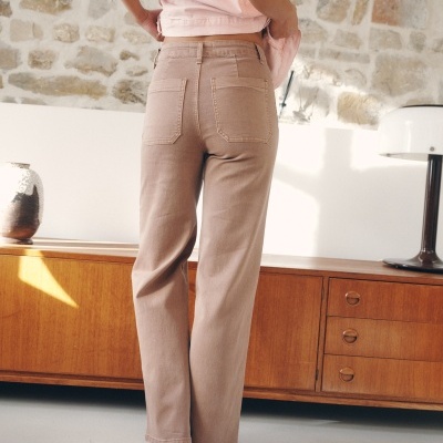 Calças castanho claro com corte direito num ambiente interior com móvel de madeira e parede de pedra