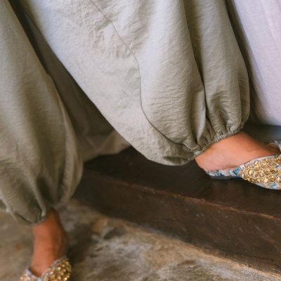 Pantalonas cinza largas com elástico nos tornozelos e sapatos bordados dourados sentada em degrau