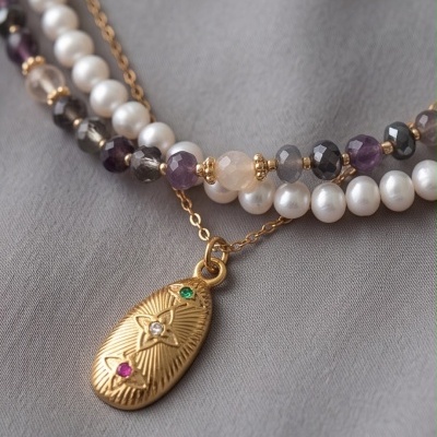 Colar duplo com pérolas e contas facetadas com pendente dourado sobre tecido cinza