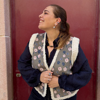 Mulher com colete floral cinzento e camisa preta contra porta vermelha