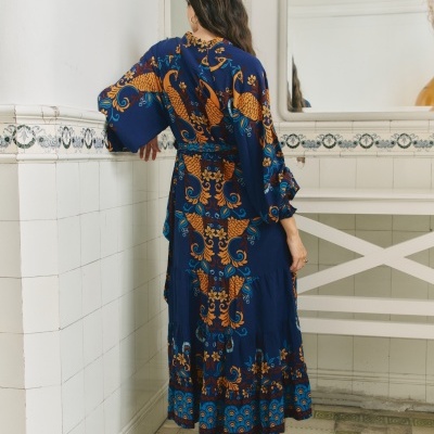 Vestido azul escuro com padrão laranja e azul claro, manga larga e folhos, visto de costas em interior com azulejos