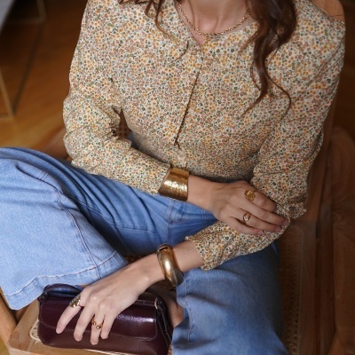 Blusa floral bege com calças de ganga e acessórios dourados numa cadeira de madeira