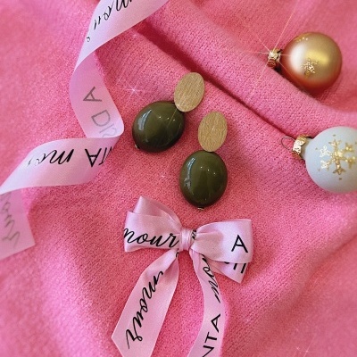 Brincos dourados e verdes com fita rosa e bolas de Natal sobre tecido rosa