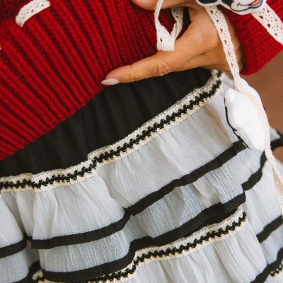 Camisola vermelha tricotada, saia branca com detalhes pretos e dourados, fita de renda bege e pendente Minnie Mouse.