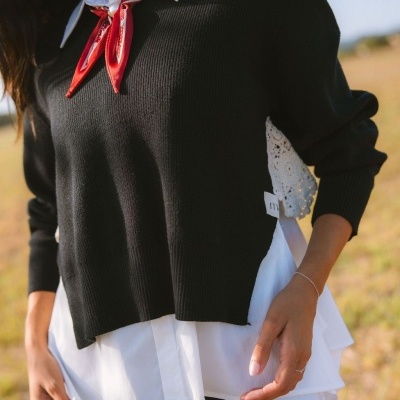Pessoa com blusão preto e camisa branca com laço vermelho e rendas brancas exteriores