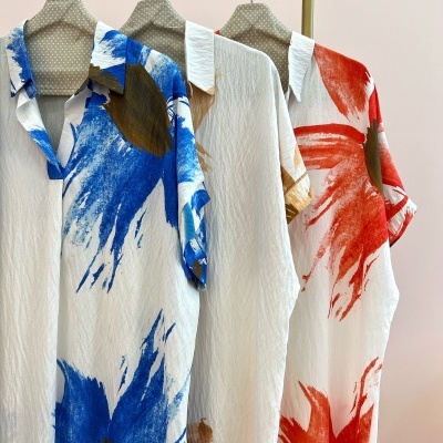 Três camisas com padrões coloridos penduradas em cabides num suporte metálico dourado.