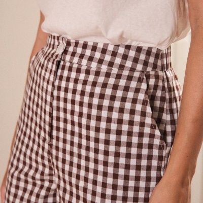 Pessoa com blusa branca e calças ou saia curta xadrez vichy castanho e branco.