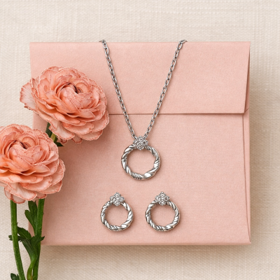 Conjunto de joalharia em prata com colar e brincos sobre envelope rosa e flores cor de pêssego