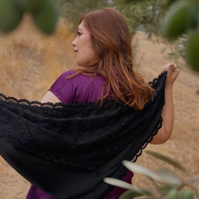 Mulher com blusa roxa e manta preta bordada ao ar livre