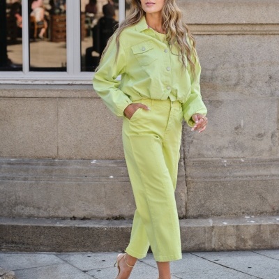 Mulher com conjunto amarelo-limão de casaco e calças, sandálias douradas e óculos de sol, em ambiente urbano