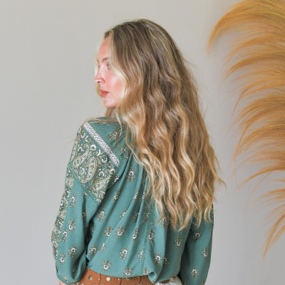 Blusa verde com padrão floral e saia branca de renda, vista de costas.