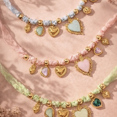 Colares com fita rendada e pendentes em formato de coração em várias cores sobre fundo rosa.