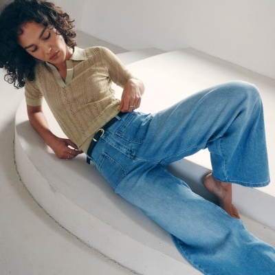 Mulher deitada com camisola bege de malha e calças de ganga largas azuis.