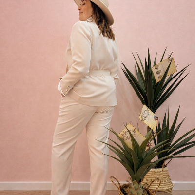 Mulher com fato creme e chapéu em fundo rosa com plantas em vasos trançados