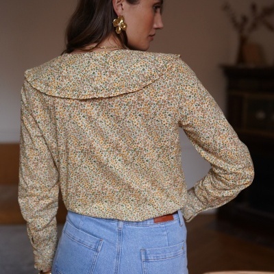 Blusa floral amarela de manga comprida com gola larga e calças de ganga azul claro vistas de costas