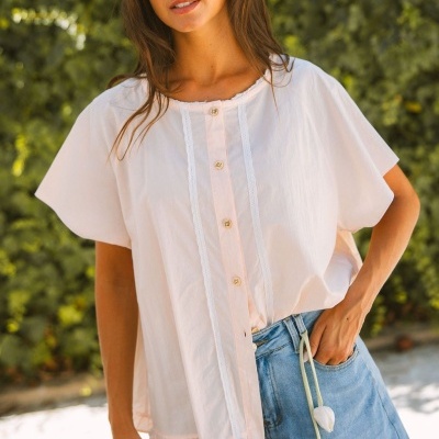 Mulher com blusa branca de botões e calças de ganga azuis, usando óculos de sol, ao ar livre