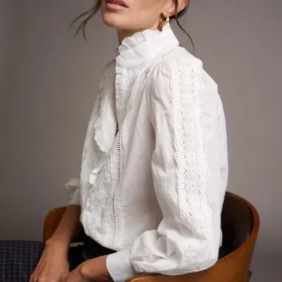 Blusa branca de tecido leve com detalhes em renda usada por mulher sentada numa cadeira