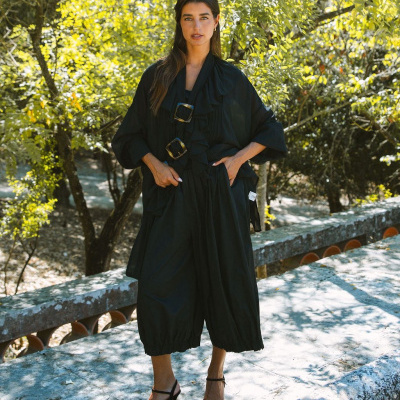 Macacão preto largo com folhos e fivelas, sandálias de salto floral feminino em ambiente natural