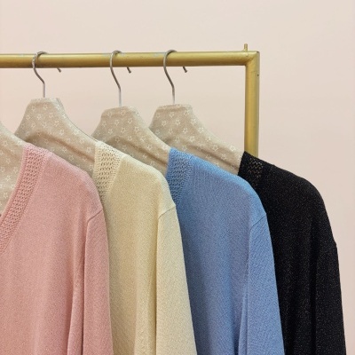 Quatro camisolas de malha em rosa, creme, azul e preto penduradas num cabideiro dourado