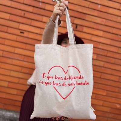 Saco de tecido bege com alças e impressão vermelha em forma de coração e texto em português.