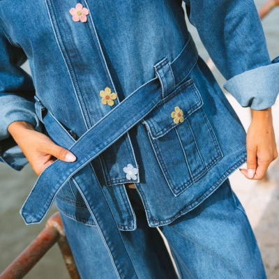 Conjunto de ganga azul com flores bordadas e cinto, usado por pessoa ao ar livre junto a estrutura metálica.