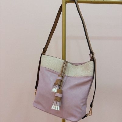 Mala de ombro rosa claro e bege com borlas pendurada em suporte metálico dourado