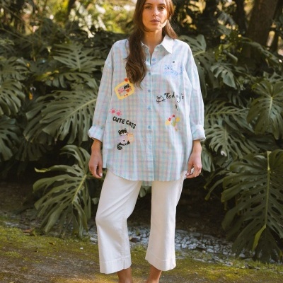 Mulher vestindo camisa azul xadrez com estampas de gatos e calças brancas ao ar livre