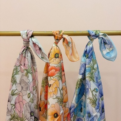 Três lenços florais coloridos pendurados num varão amarelo contra parede bege.