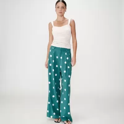 Mulher com blusa creme de alças e calças verdes de bolinhas brancas