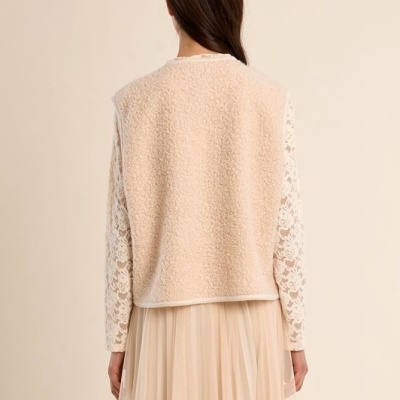 Mulher de costas com casaco bege, blusa branca de renda e saia comprida bege.