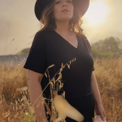 Mulher com chapéu preto e t-shirt preta em campo ao entardecer.