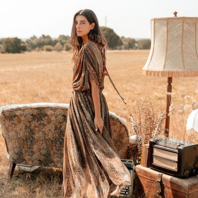 Vestido comprido com padrão animal print castanho worn por mulher, sofá floral, lâmpada e rádio vintage em campo aberto