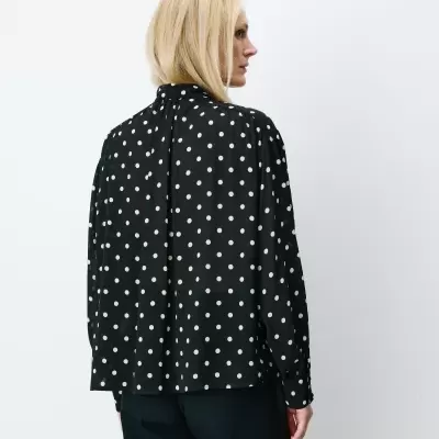 Camisa preta de bolinhas brancas vista de costas com calças pretas.