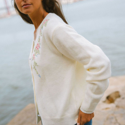 Cardigan branco com bordado floral usado por mulher à beira de água