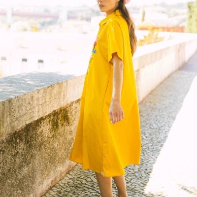 Vestido amarelo com aplicações florais usado ao ar livre com muro e calçada portuguesa.