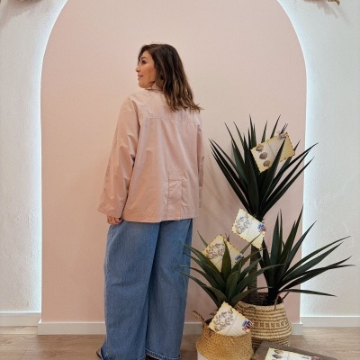 Mulher de costas com casaco bege e calças de ganga largas junto a plantas em vasos de palha