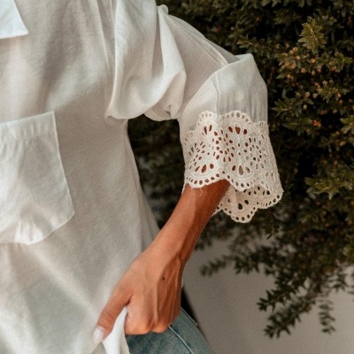 Blusa branca com manga 3/4 e renda delicada, calças de ganga azul claro, plantas verdes ao fundo