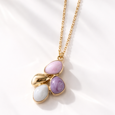 Colar dourado com pingente de pedras em tons lilás, branco e dourado sobre fundo branco
