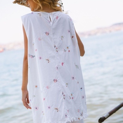 Top branco com bordados florais e chapéu de palha junto à água