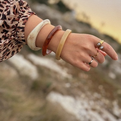 Braço com pulseiras bege, castanho, marfim e anéis dourados e prata com pedras ovais