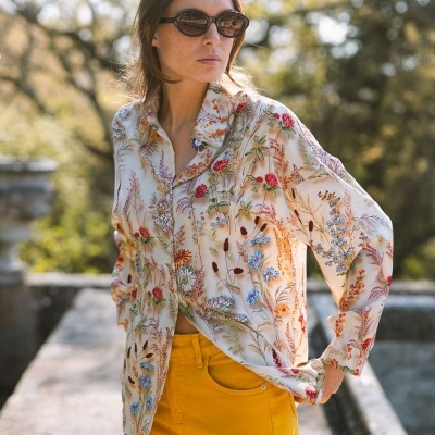 Mulher usando camisa floral creme e calças amarelas ao ar livre
