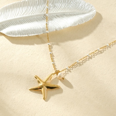 Colar dourado com pendente estrela do mar e pérola sobre fundo bege e decoração branca