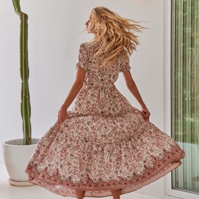 Mulher de costas com vestido comprido floral esvoaçante no interior junto a cactos e luz de parede