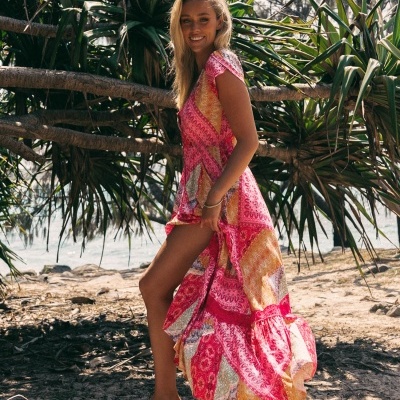 Vestido longo colorido feminino com padrão étnico numa praia, mulher descalça.